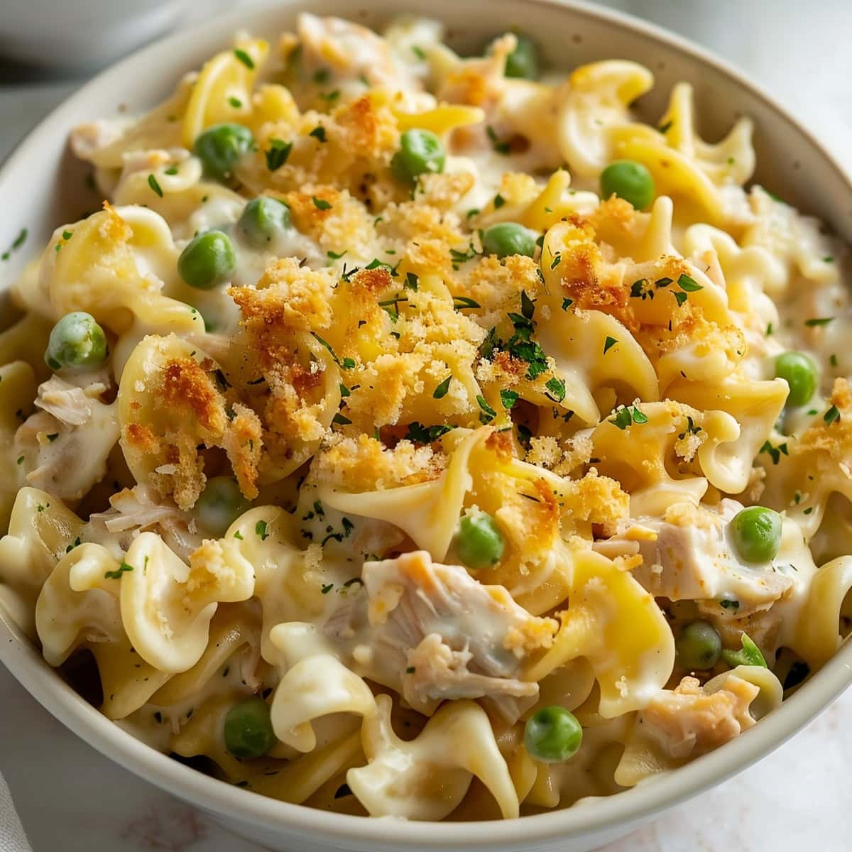 A bowl of rich and creamy tuna and noodles with green peas.
