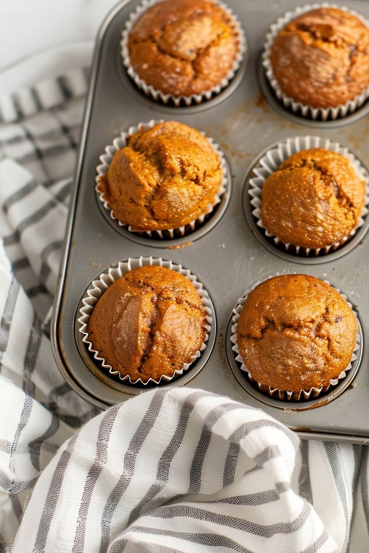 Close Up of Two-Ingredient Pumpkin Muffins in Liners in a Muffin Tray with  Striped Kitchen Towel