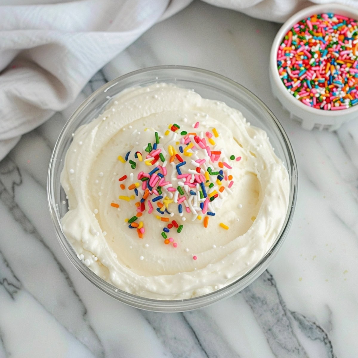 A glass bowl of funfetti cake dip with rainbow sprinkles on the side.