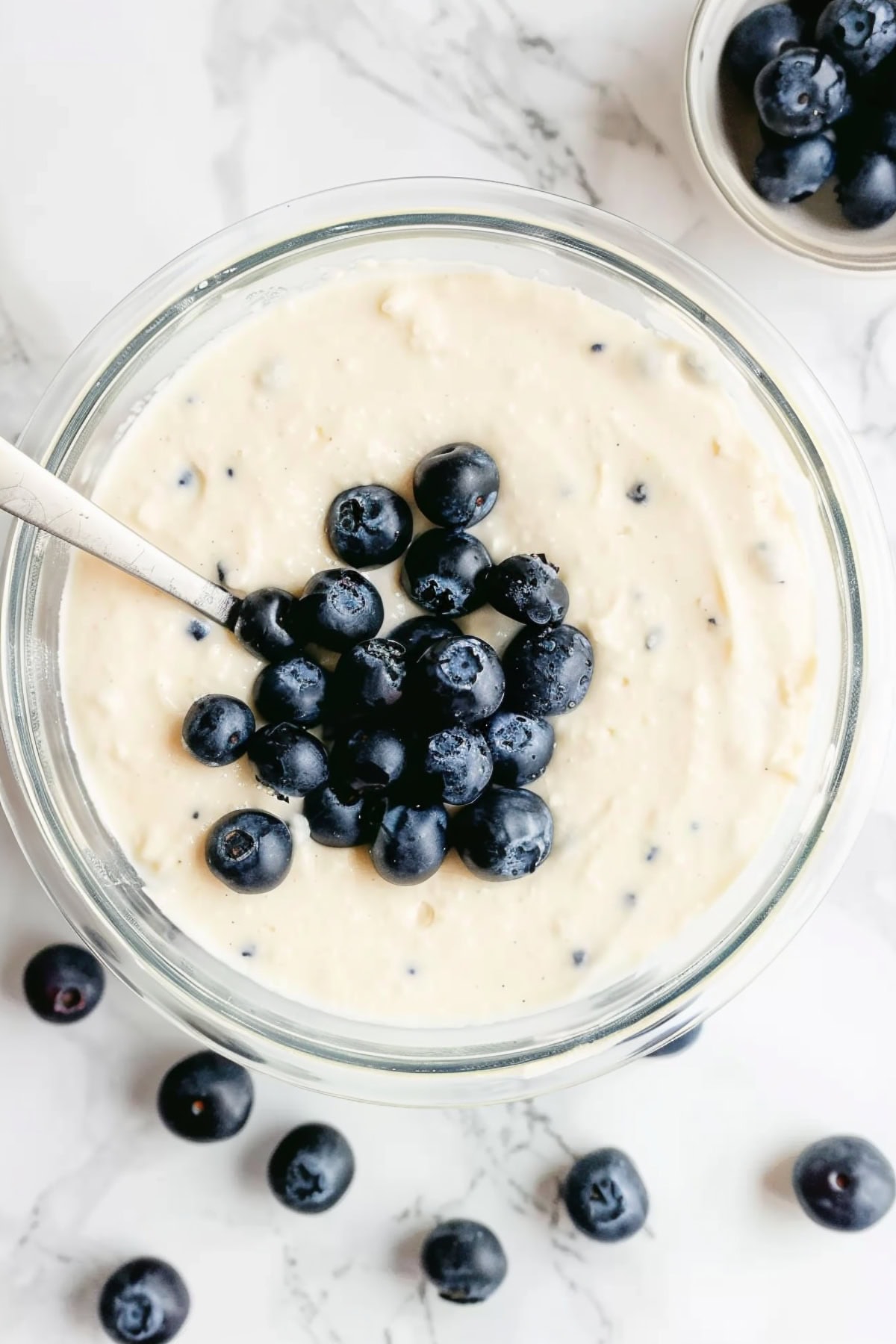 A glass bowl of white batter topped with fresh blueberries.