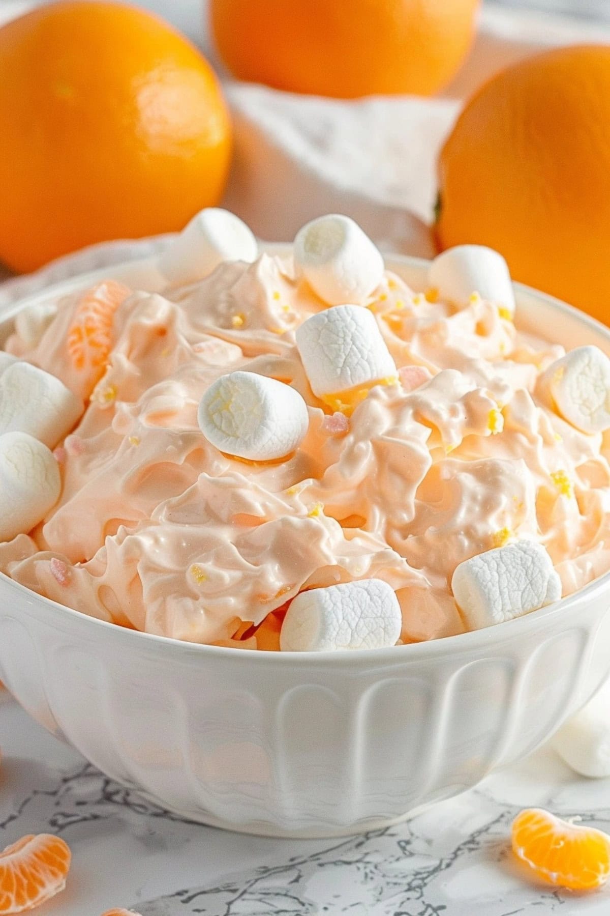 Orange fluff salad served in a white bowl with marshmallow garnish.