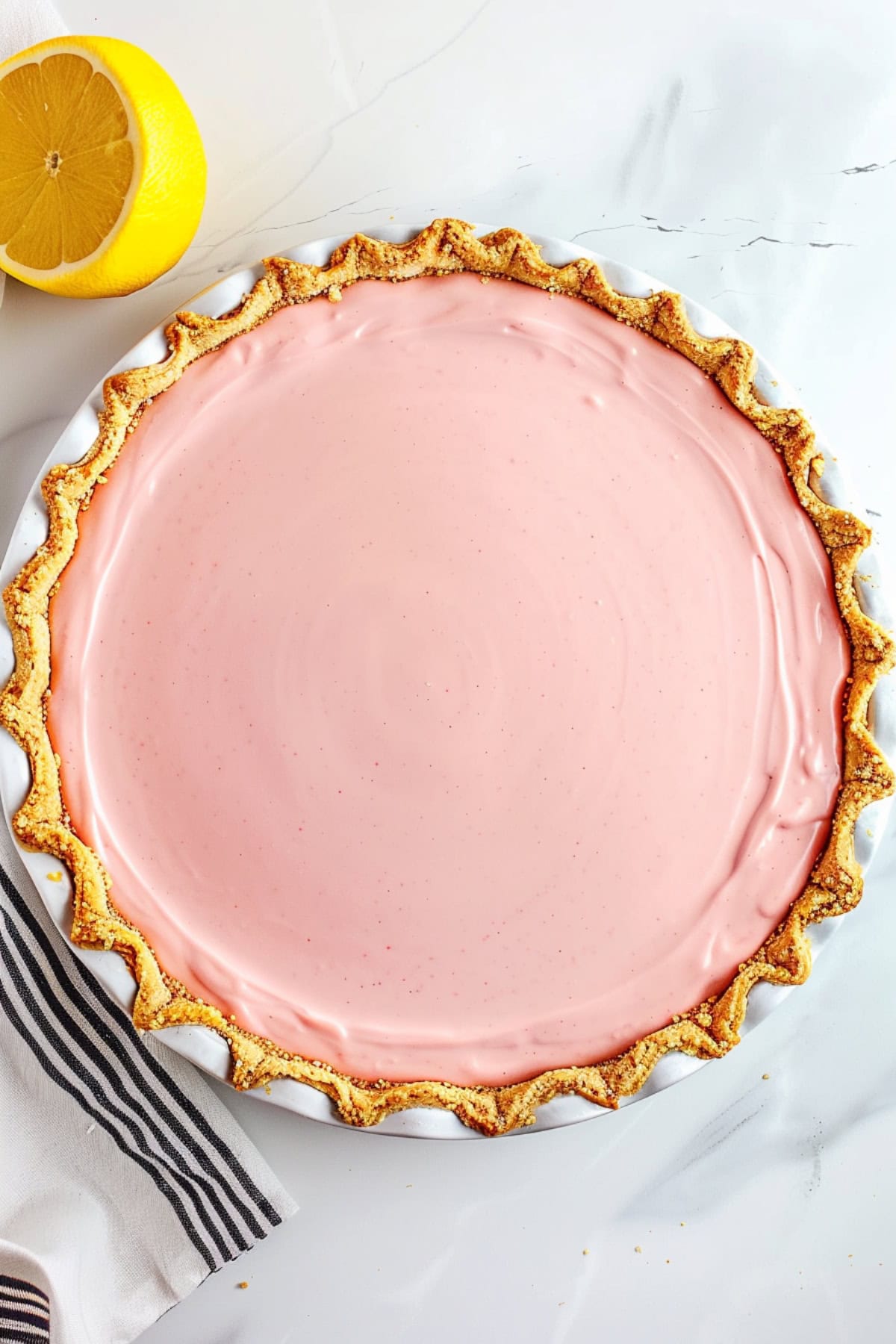 Top view of a whole pink lemonade pie with fresh lemon on the side.