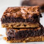 Two Stacked Gooey, Fudgy Brookies with Brownie Top Layer and Chocolate Chip Cookie Bottom Layer on a White Marble Table with Chocolate Chips Around the Brownies