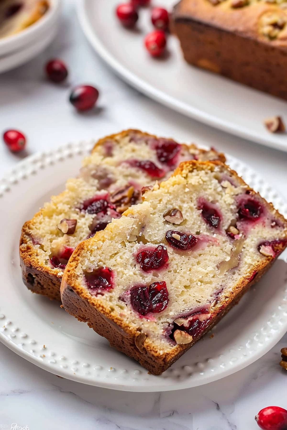 Close Up of Two Slices of Cranberry Orange Bread with Chunks of Cranberries and Walnuts on a White Plate