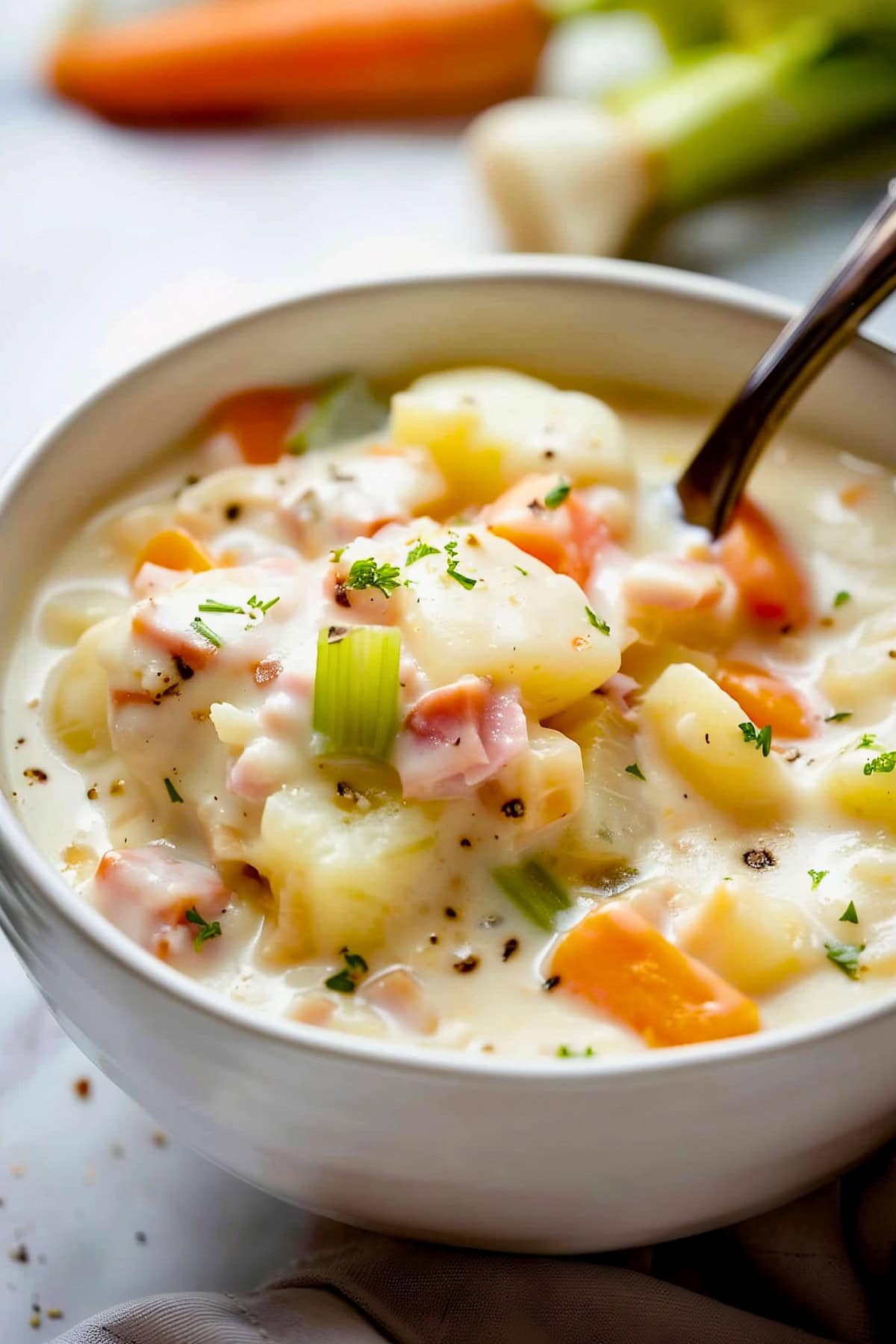 Creamy Ham and Potato Soup with Chunk so Ham, Potatoes, Carrots, Celery, and Seasonings in a Bowl with a Spoon