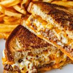 Close Up of Gooey, Cheesy, Meaty Patty Melt with Crispy Bread on a White Plate with French Fries