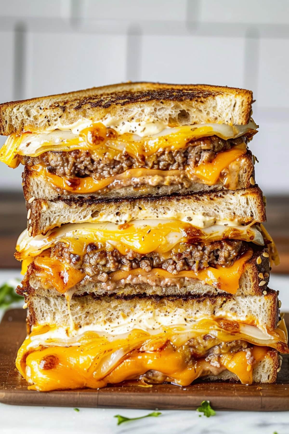 Three Cut Halves of Patty Melts with Gooey Cheese and Juicy Burgers Stacked on a Wooden Cutting Board