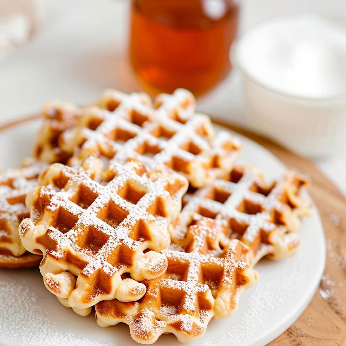 Waffle Cookies Dusted with Powdered Sugar on a White Plate on a Wooden Cutting Board with Honey and Milk in the Background
