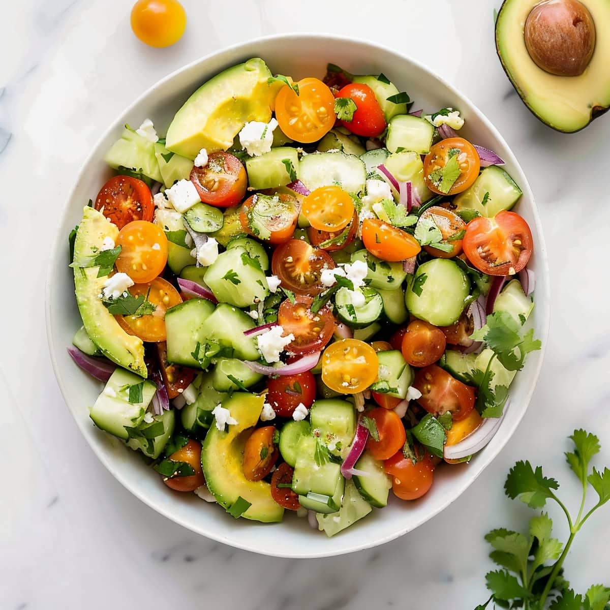 A bowl of fresh salad with avocado slices, cucumbers, cherry tomatoes and crumbled feta.