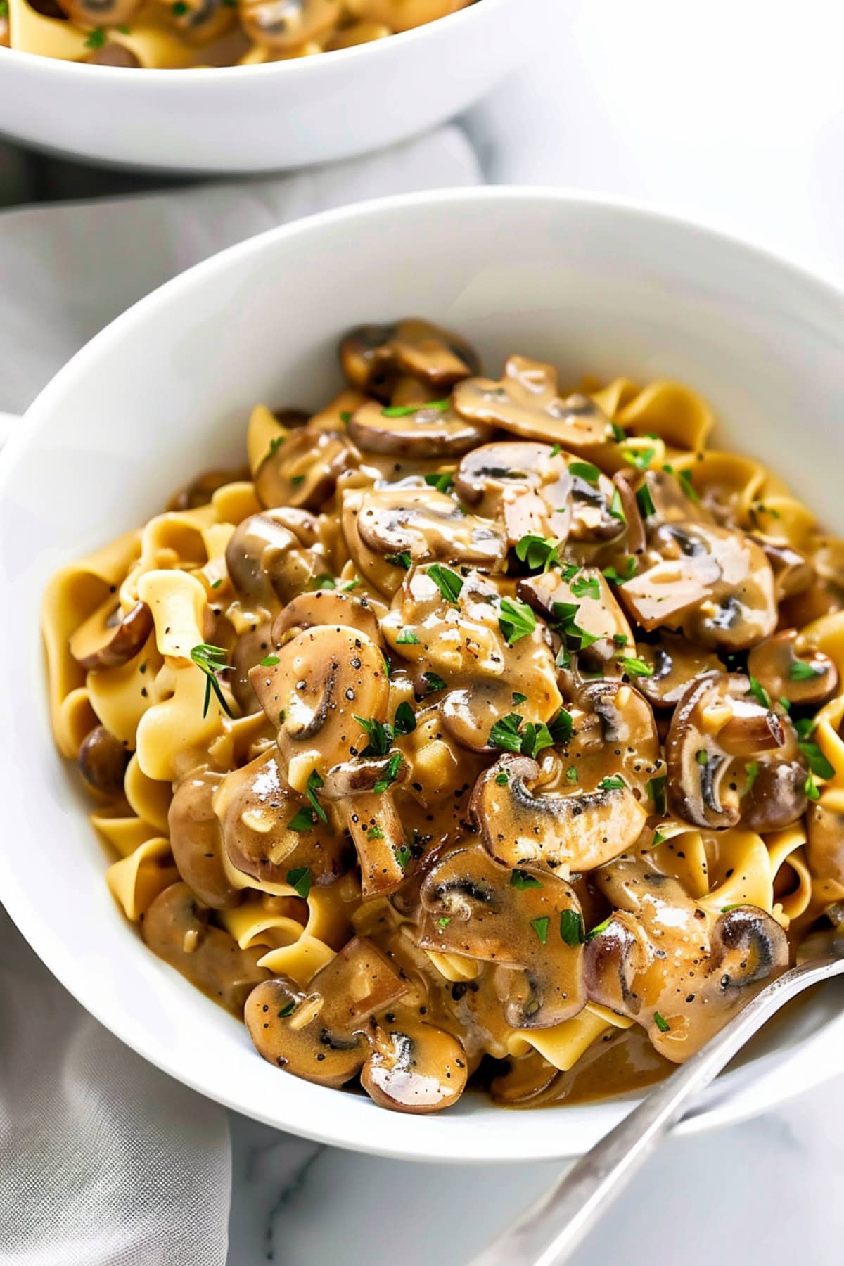 A close-up of a creamy mushroom stroganoff served over a bed of egg noodles, garnished with fresh parsley.