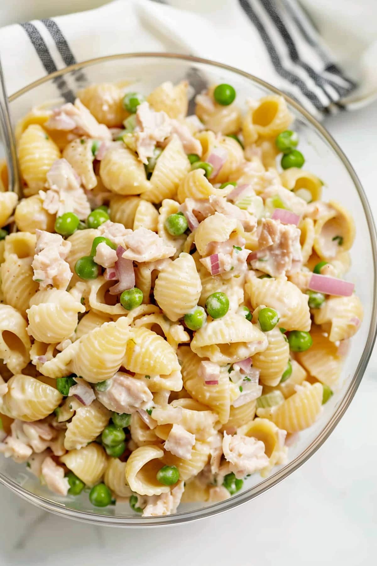 Tuna pasta salad with red onions and green peas in a glass bowl.