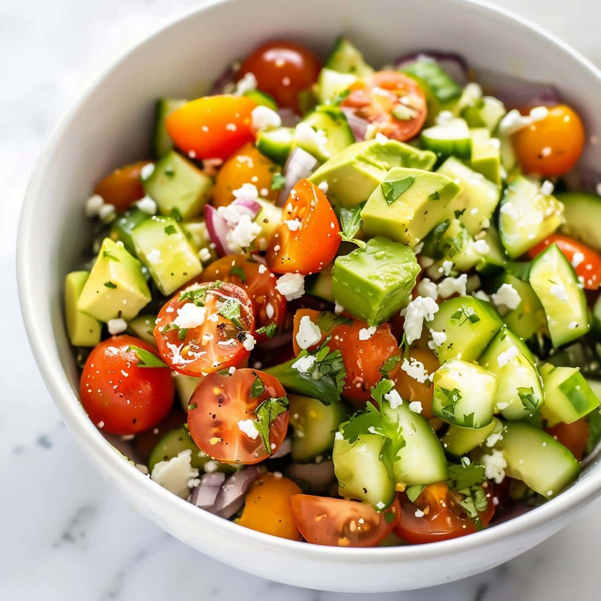 Close-up shot of healthy avocado salad with cherry tomatoes, cucumbers, red onions and feta.