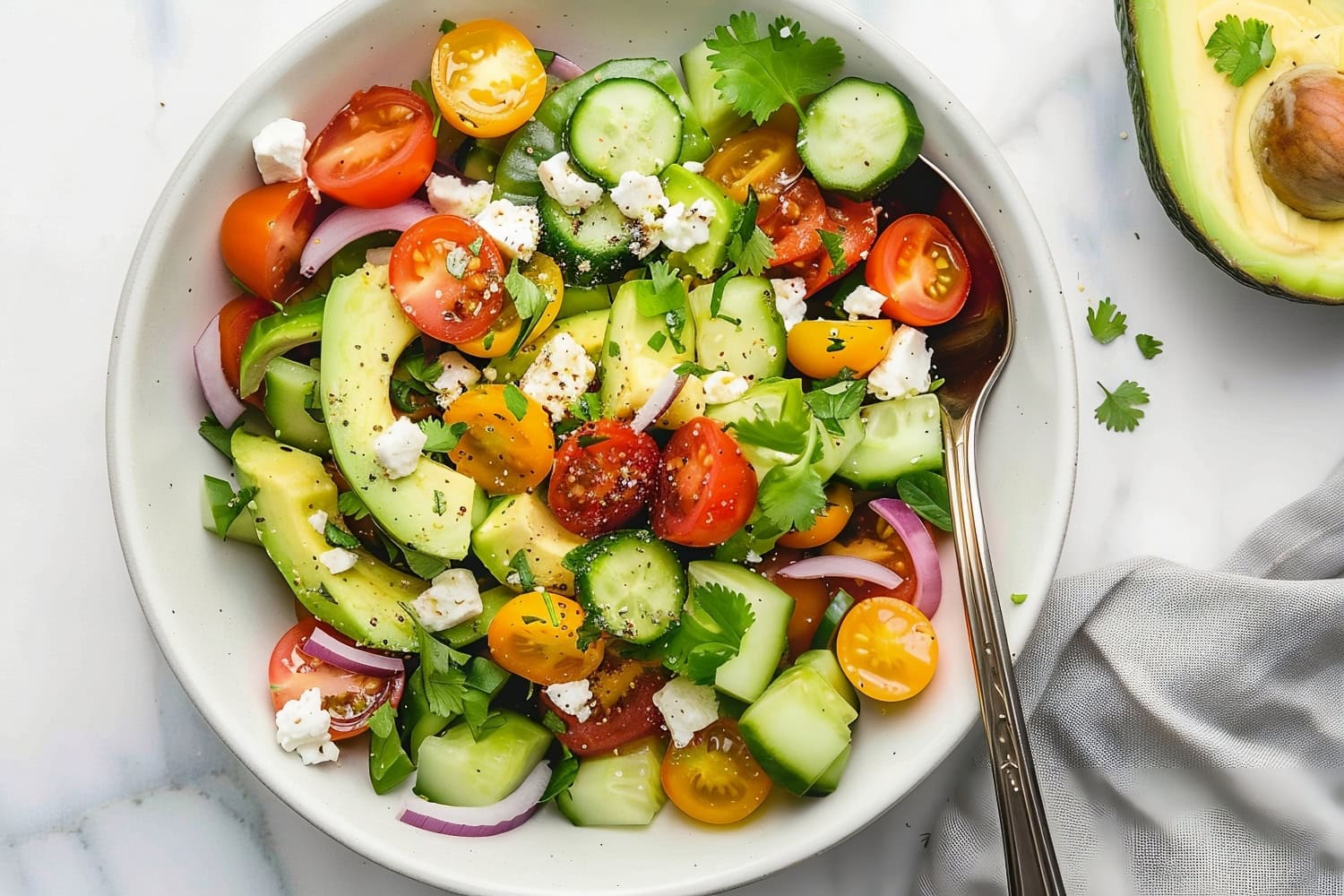 Simple avocado salad in a bowl with cherry tomatoes, feta, cucumbers and red onions.