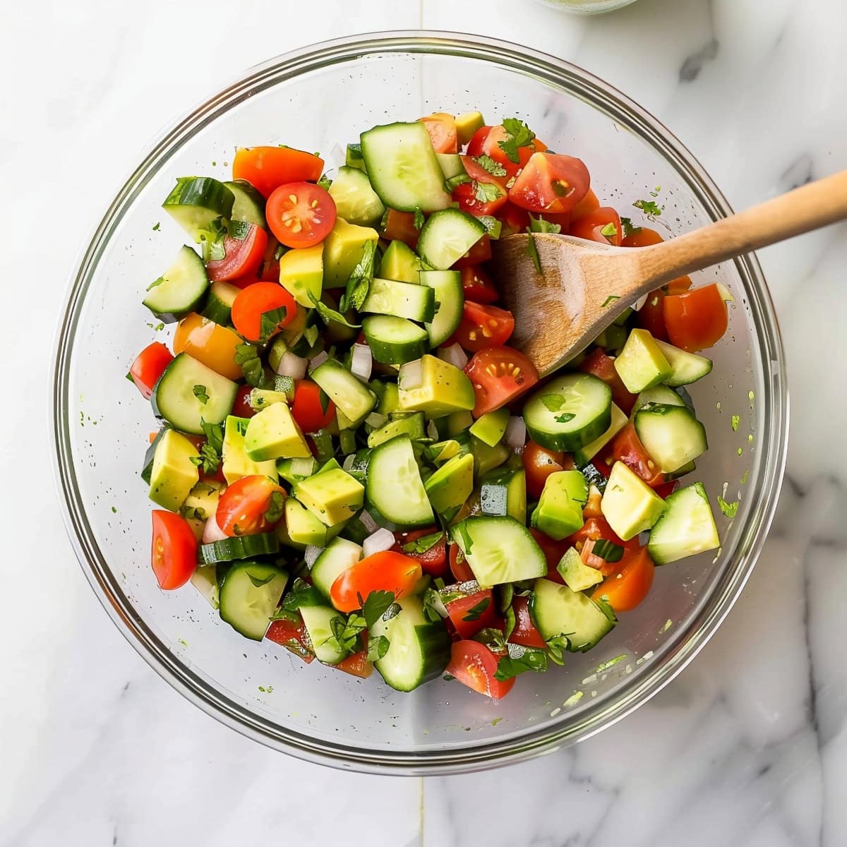 A glass bowl of avocadoes, tomatoes, cherry tomatoes and cilantro.