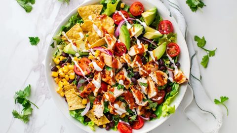 Colorful BBQ chicken salad featuring grilled chicken, black beans, corn, avocado, and cherry tomatoes on a bed of lettuce.