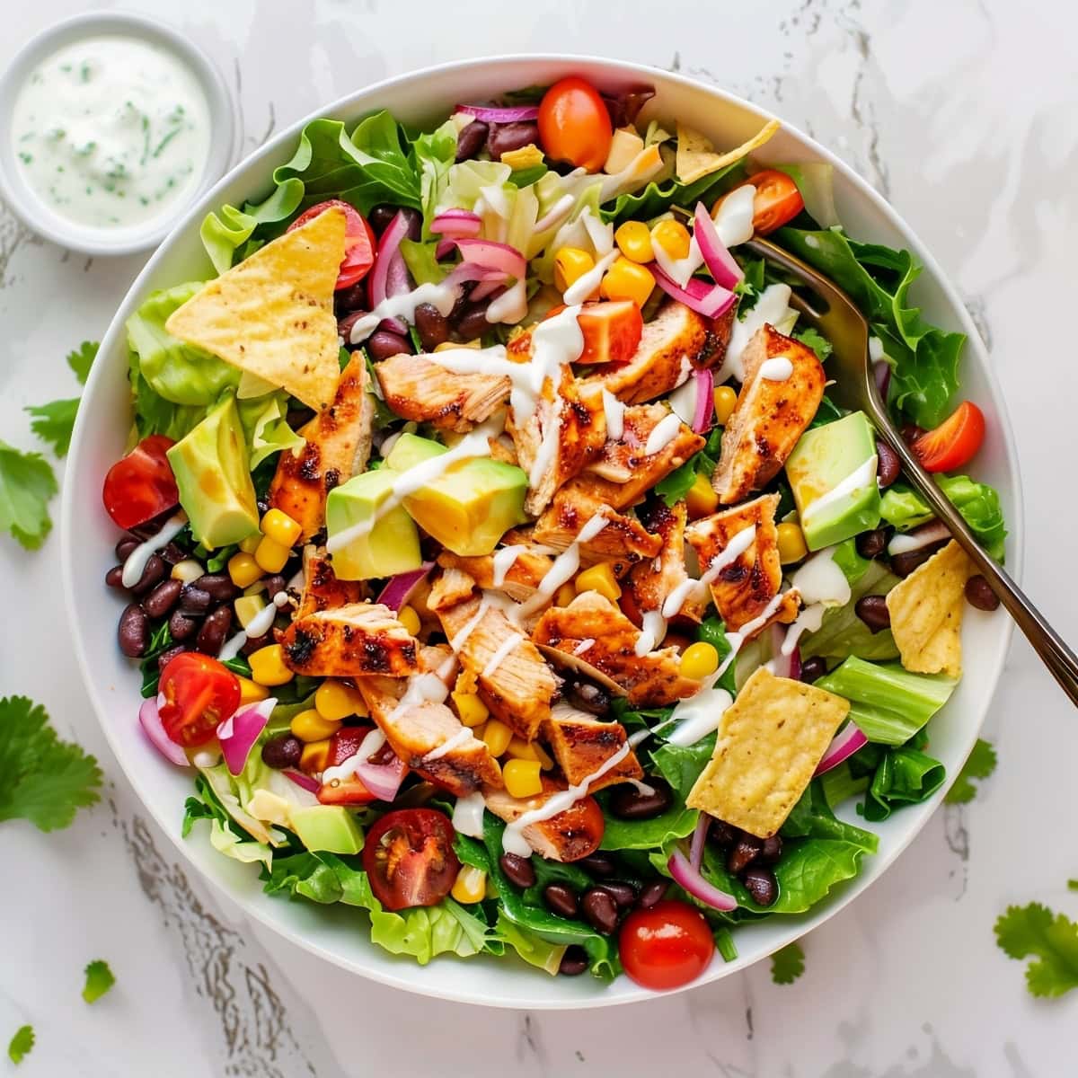 A delicious BBQ chicken salad in a white bowl, garnished with cherry tomatoes, red onions, and avocado chunks.