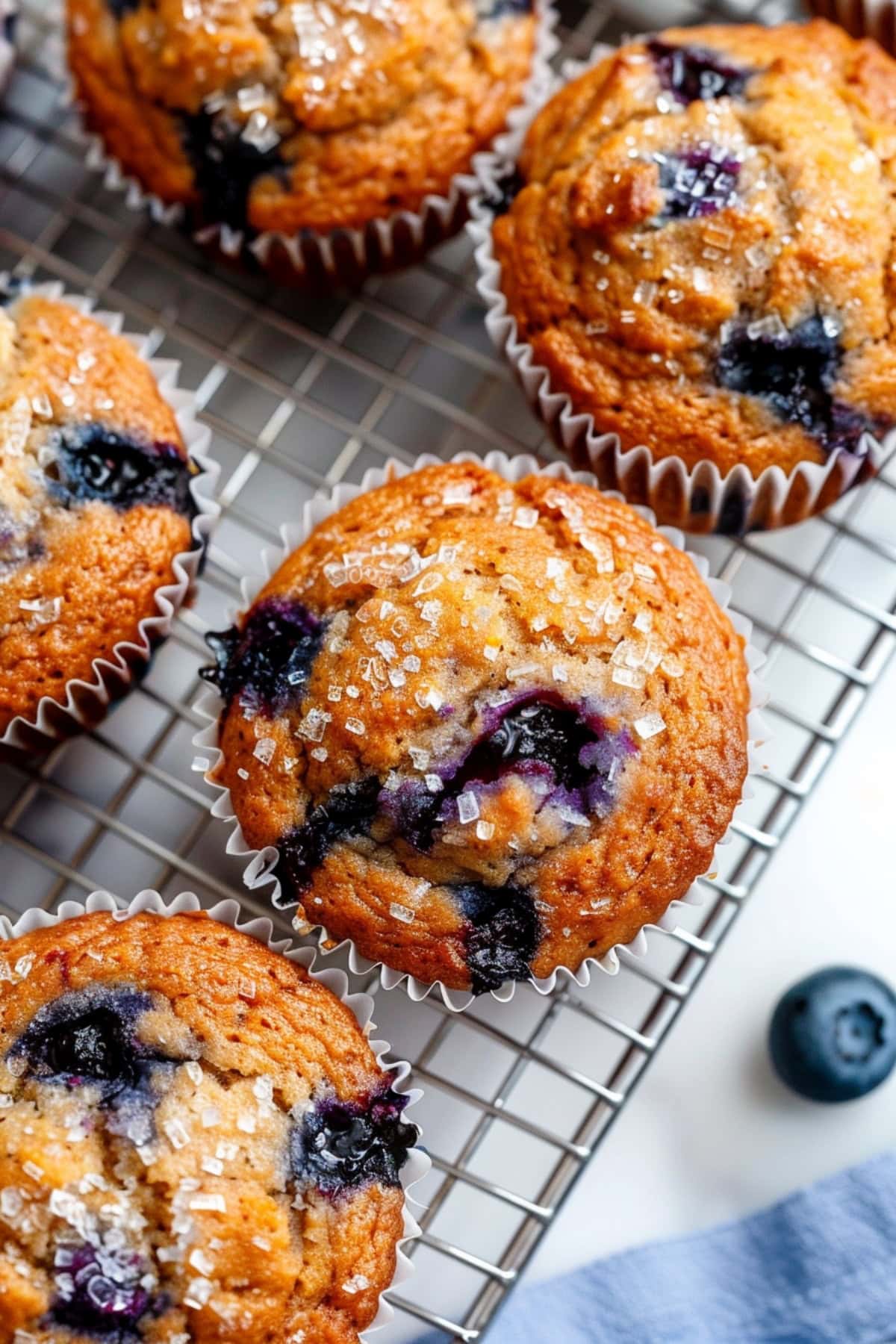 Moist homemade banana blueberry muffins on a cooling rack on a white marble table, top view