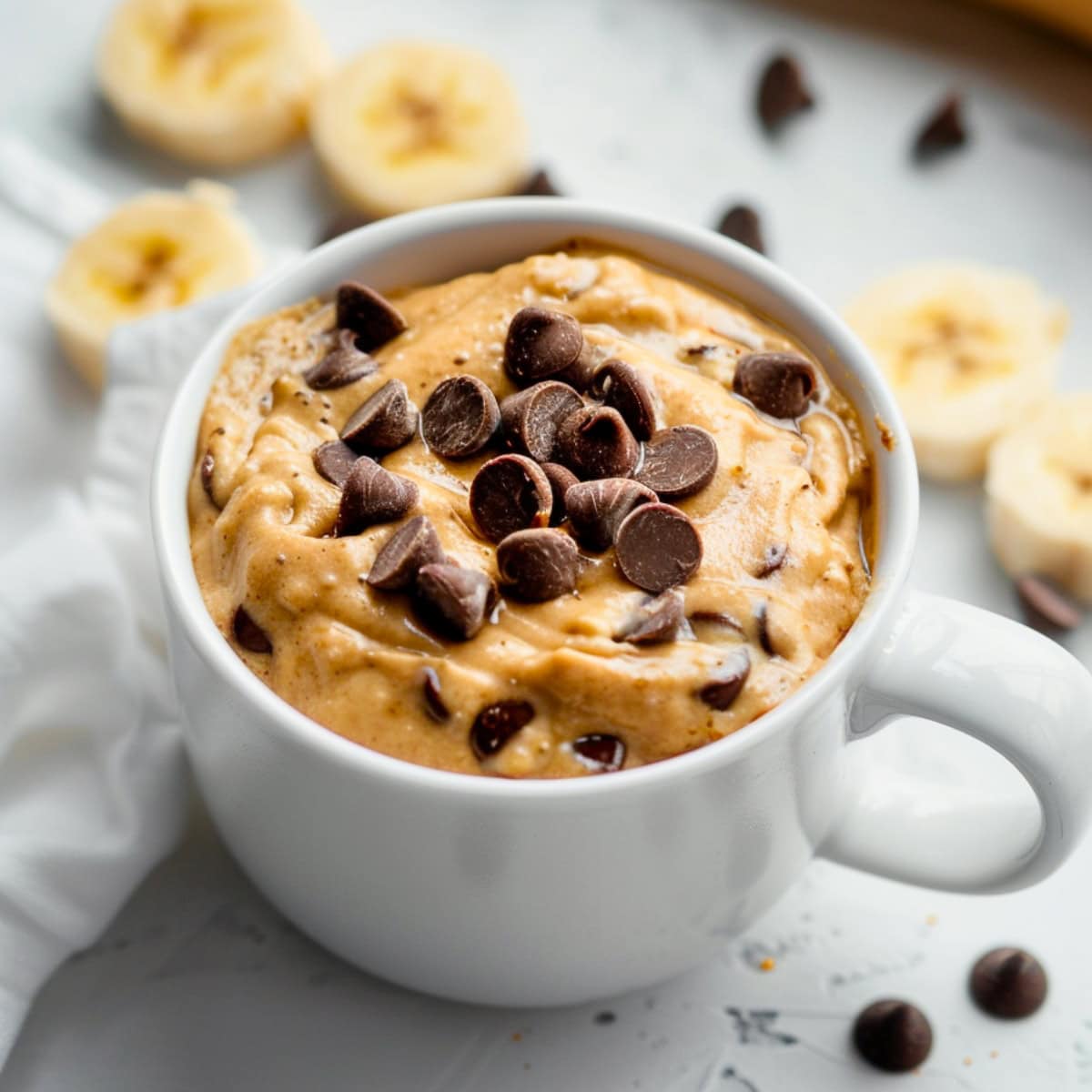 Banana cake batter topped with chocolate chips in a white mug.
