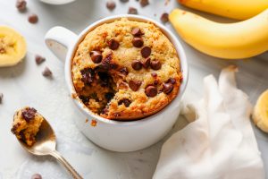 Banana bread baked inside a white mug topped with chocolate chips.