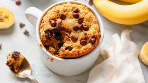 Banana bread baked inside a white mug topped with chocolate chips.