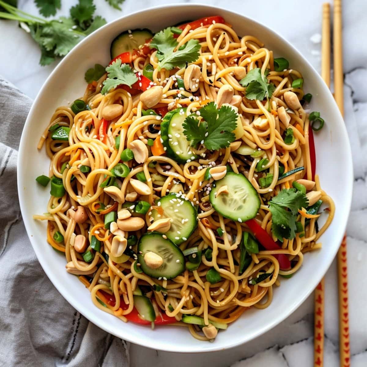 Elegant Asian noodle salad garnished with chopped peanuts, fresh cilantro, cucumber and carrots.