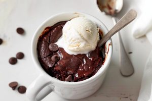 Brownie in a mug garnished with a scoop of vanilla ice cream.