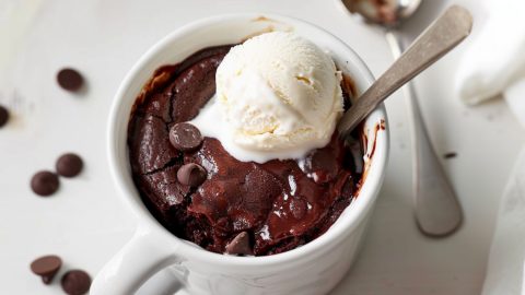 Brownie in a mug garnished with a scoop of vanilla ice cream.