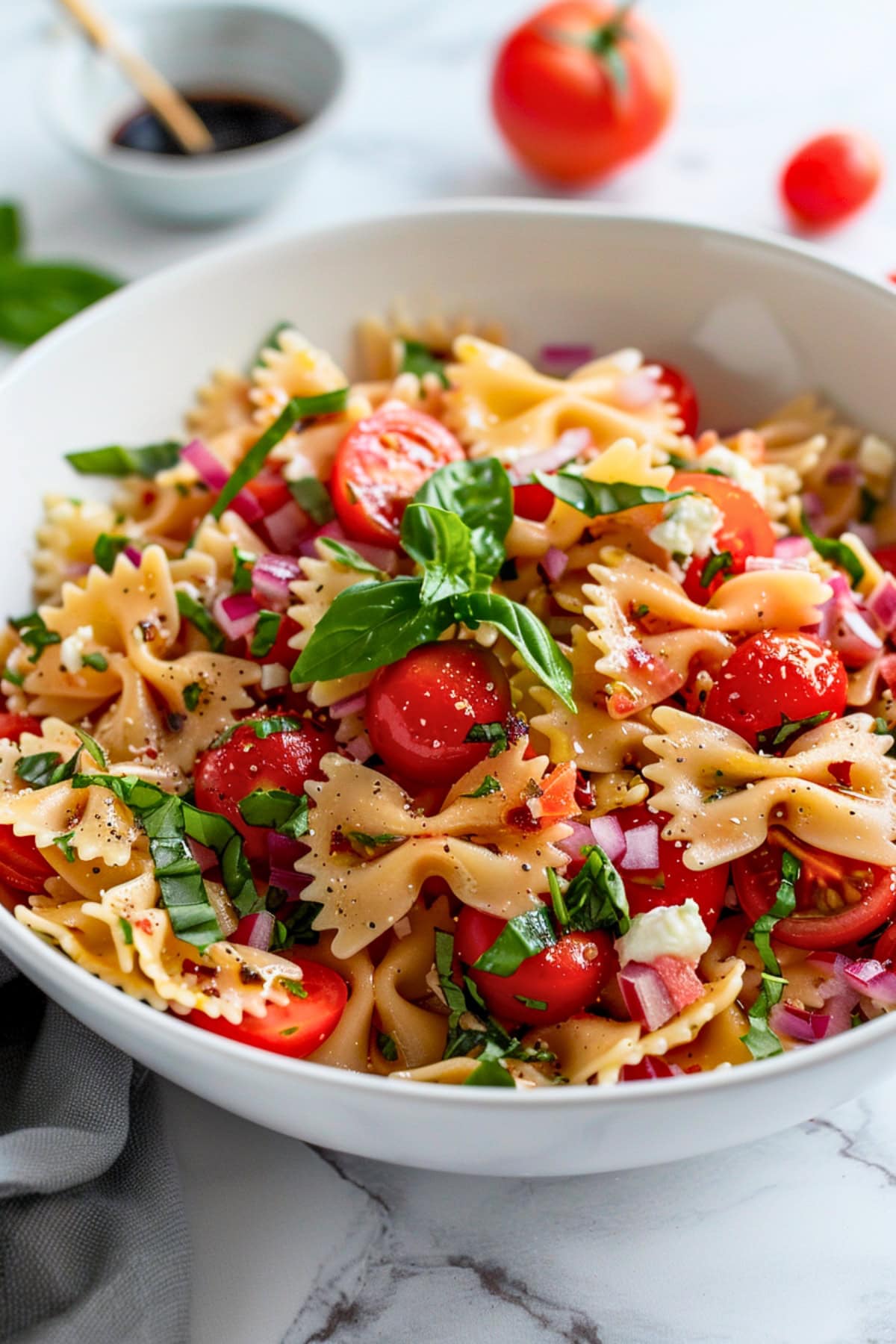 Bruschetta pasta salad made with made with cherry tomatoes, fragrant basil, tangy balsamic vinegar, and creamy mozzarella pearls and bowties pasta served in a white bowl.