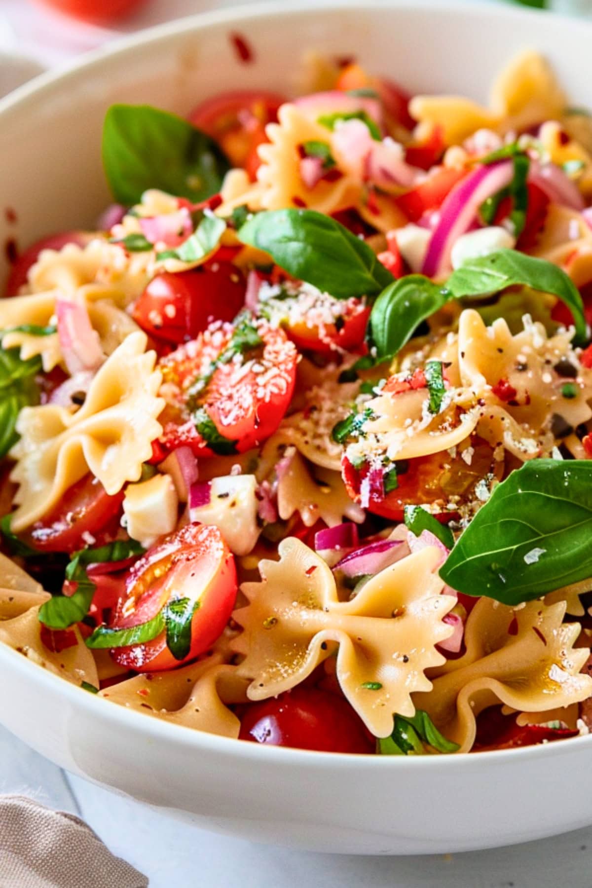 Pasta salad made with  cherry tomatoes, fragrant basil, tangy balsamic vinegar, and creamy mozzarella pearls and bowties pasta served in a white bowl.