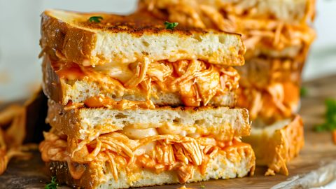 Grilled cheese sandwich with buffalo chicken filling on a wooden cutting board.