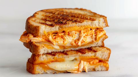 A closeup photo of a grilled cheese sandwich with buffalo chicken, sitting on top of each other and cut in half to show the filling.