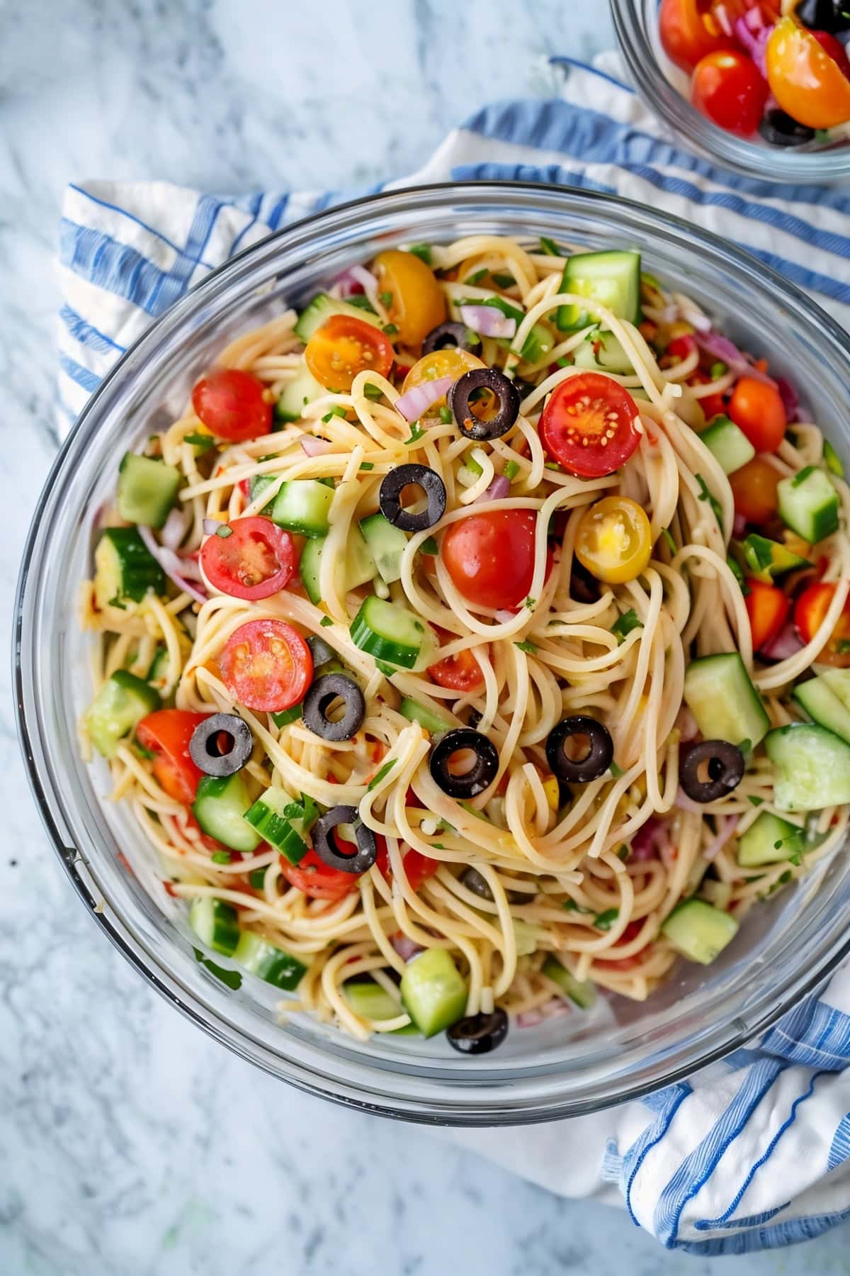 Colorful homemade California spaghetti salad with cherry tomatoes, diced cucumbers and chopped olives.