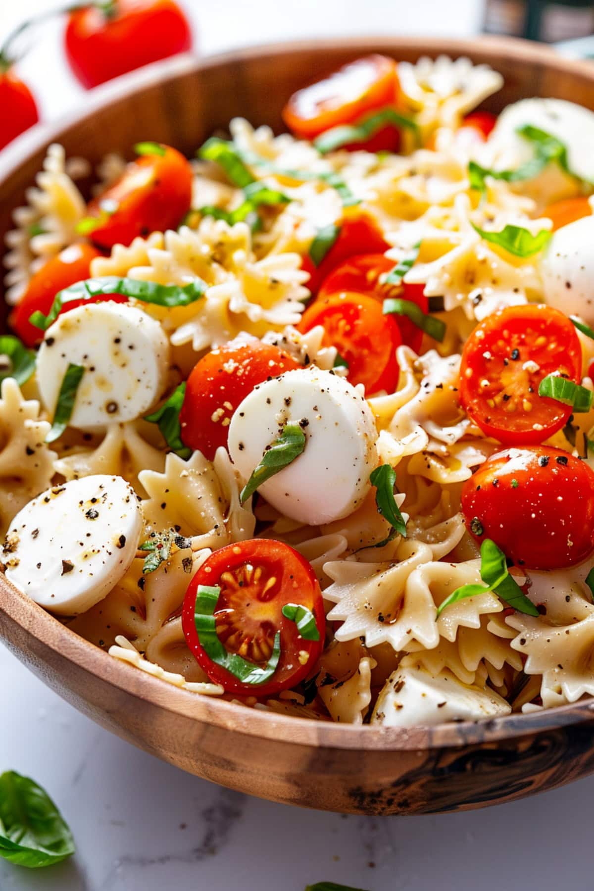 Caprese pasta salad with farfelle pasta, cherry tomatoes, basil and caprese cheese with dressing served on a wooden bowl.