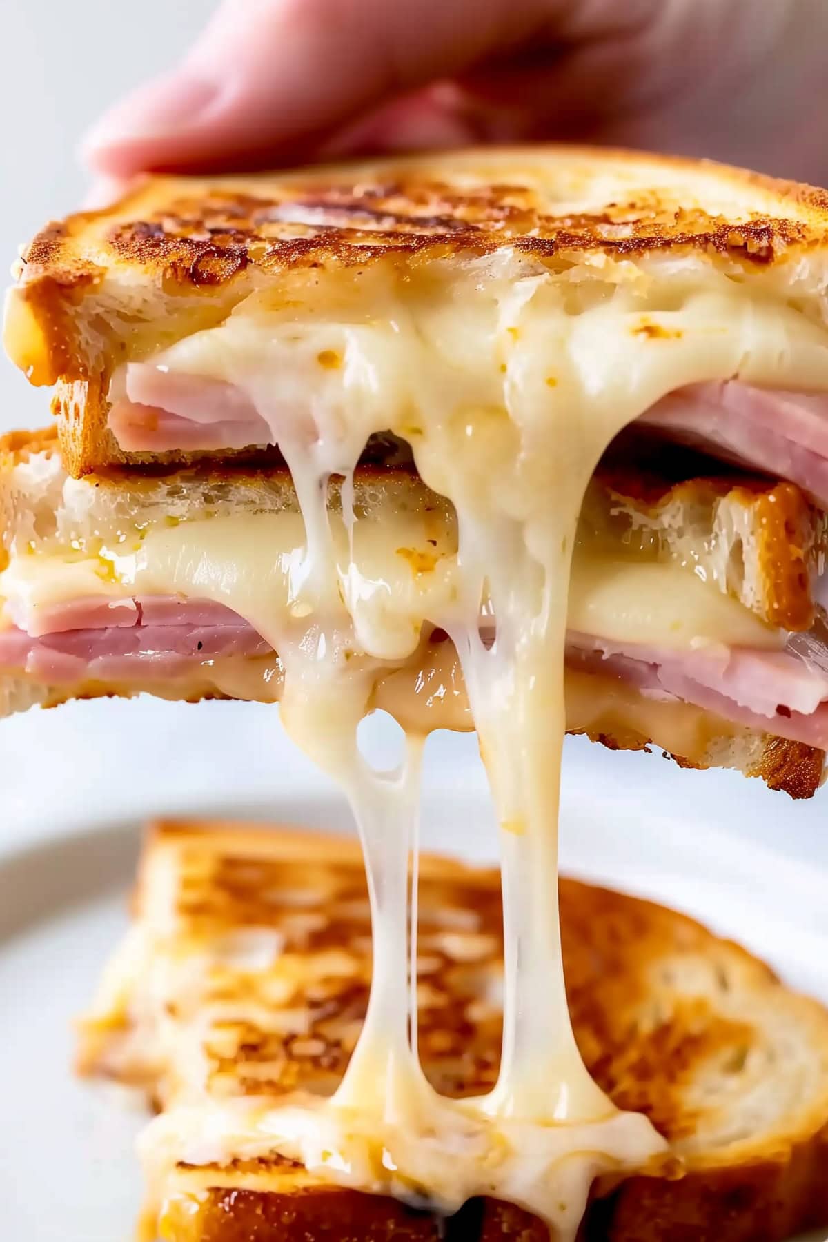 A grilled ham and cheese sandwich held in hand, with melted cheese stretching out from the bite.