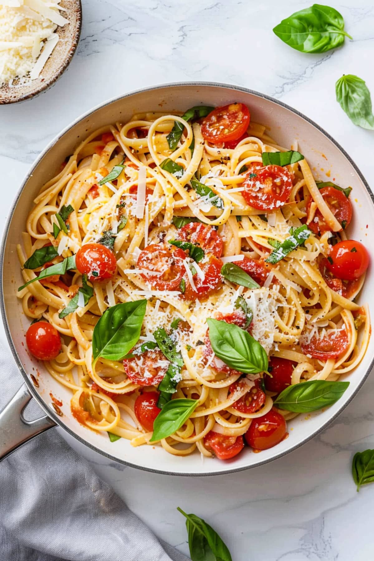 Cherry tomato and linguine pasta with fresh basil leaves in a saucepan.