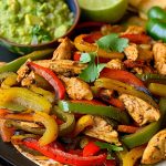 Close Up of Chicken Fajitas -Chicken, Peppers, and Onions in Spices- on a Plate with Guacamole and Limes