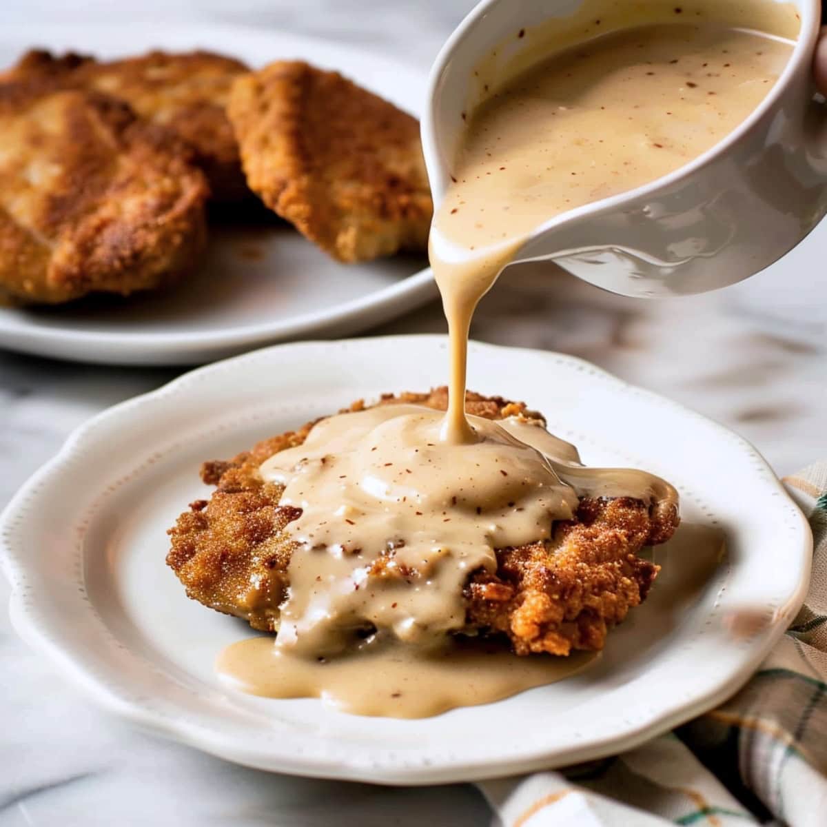 Gravy poured into a chicken fried steak in a white plate.
