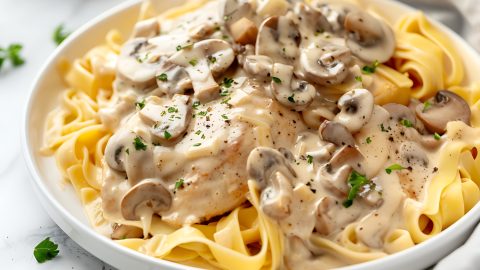 Chicken stroganoff served on top of egg noodles on a white plate.