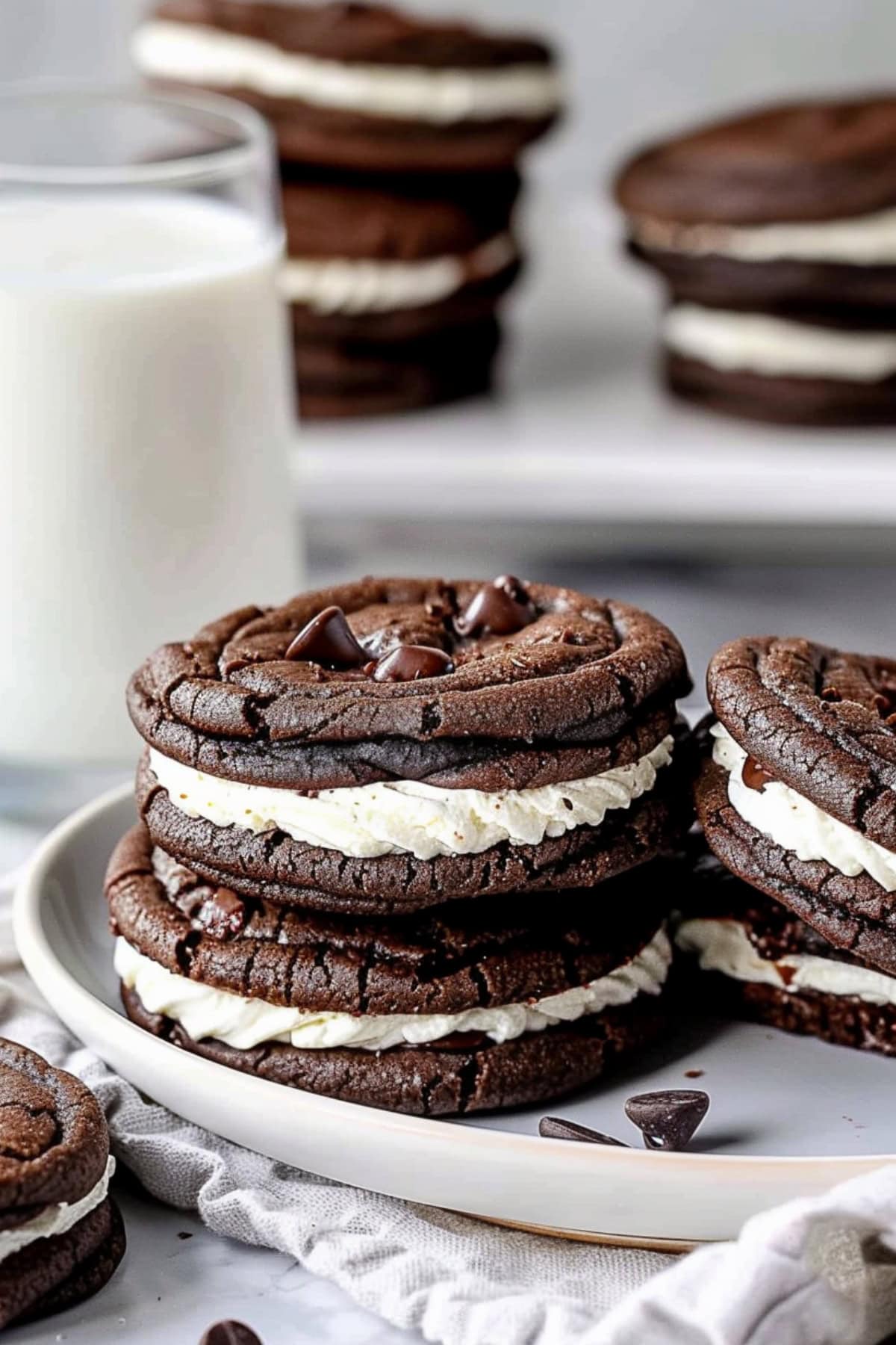 Chocolate sandwich cookies with creamy vanilla filling on a white plate with a glass of milk on the side