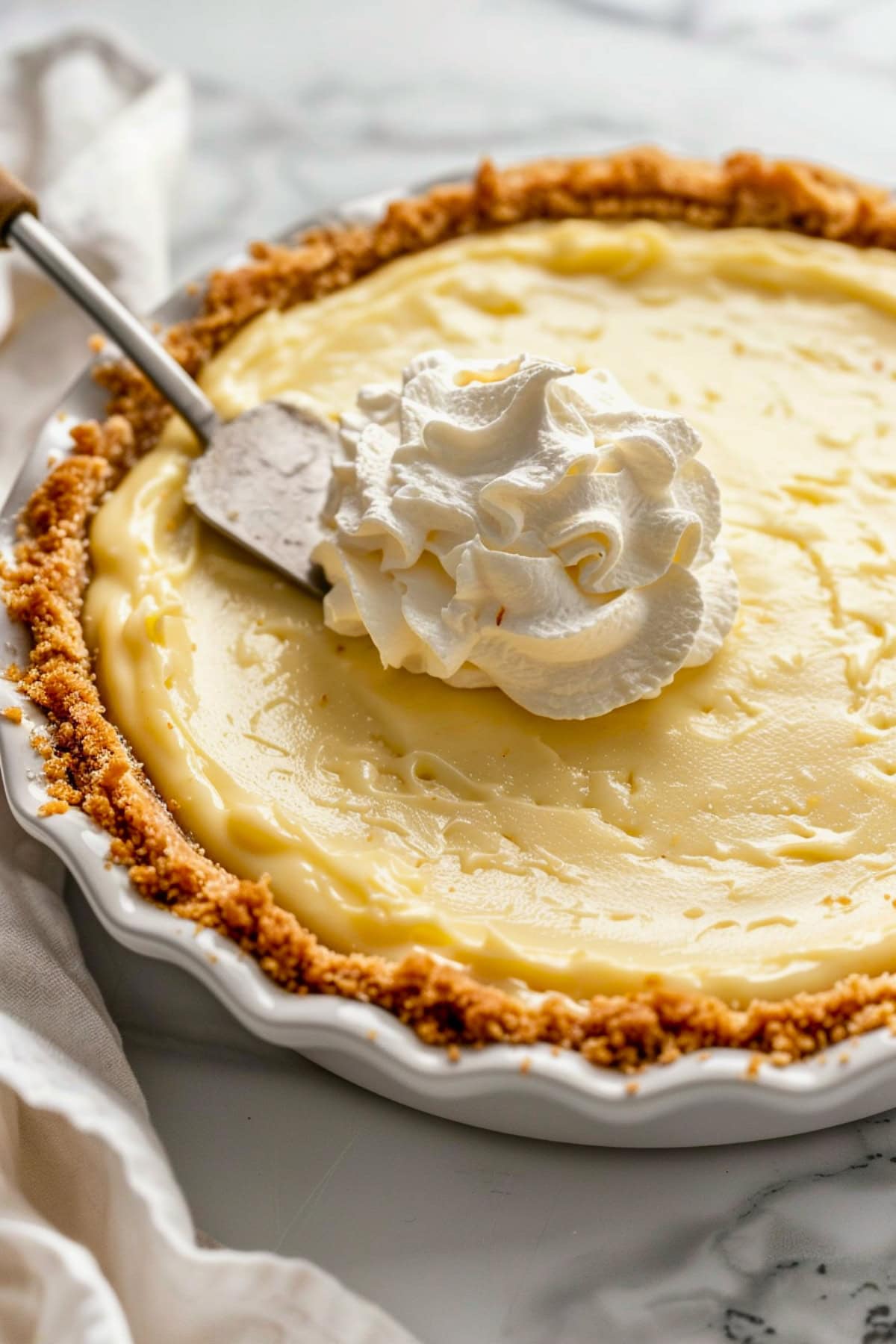 Whipped cream spread on top of coconut cream pie in a pie dish.