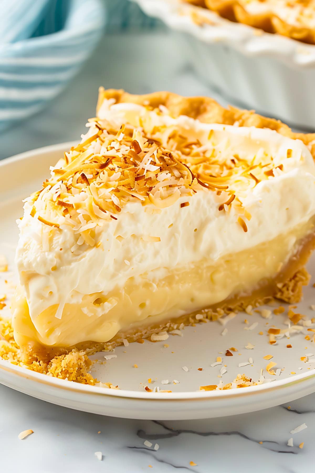 Slice of coconut cream pie served on a white plate garnished with coconut shavings on top.