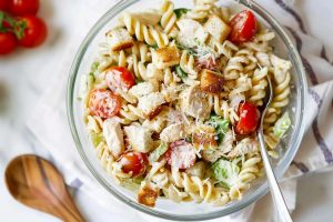 A colorful chicken Caesar pasta salad with vibrant greens, red cherry tomatoes and creamy dressing.