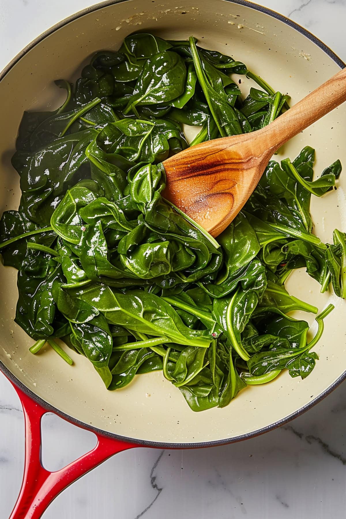 Top view of cooked baby spinach in a skillet with wooden spoon.