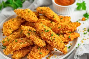 Bunch of chicken tenders coated in cornflakes arranged in a white plate.