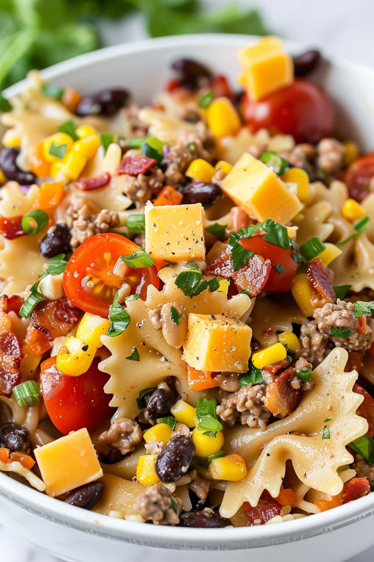Cooked pasta, ground beef, bacon, corn, black beans, tomatoes, cheddar cheese, green onions, and cilantro mixed in a bowl.