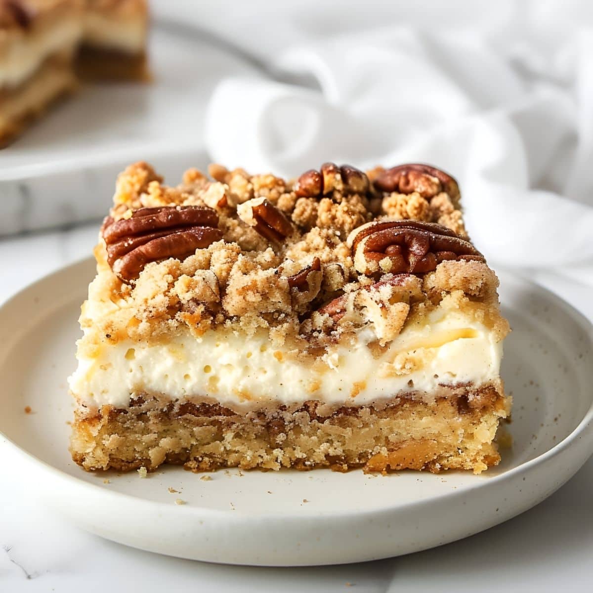 Close Up Slice of Cream Cheese Coffee Cake with Layers of Cheesecake, Coffee Cake, and Crumble Topping on a White Plate
