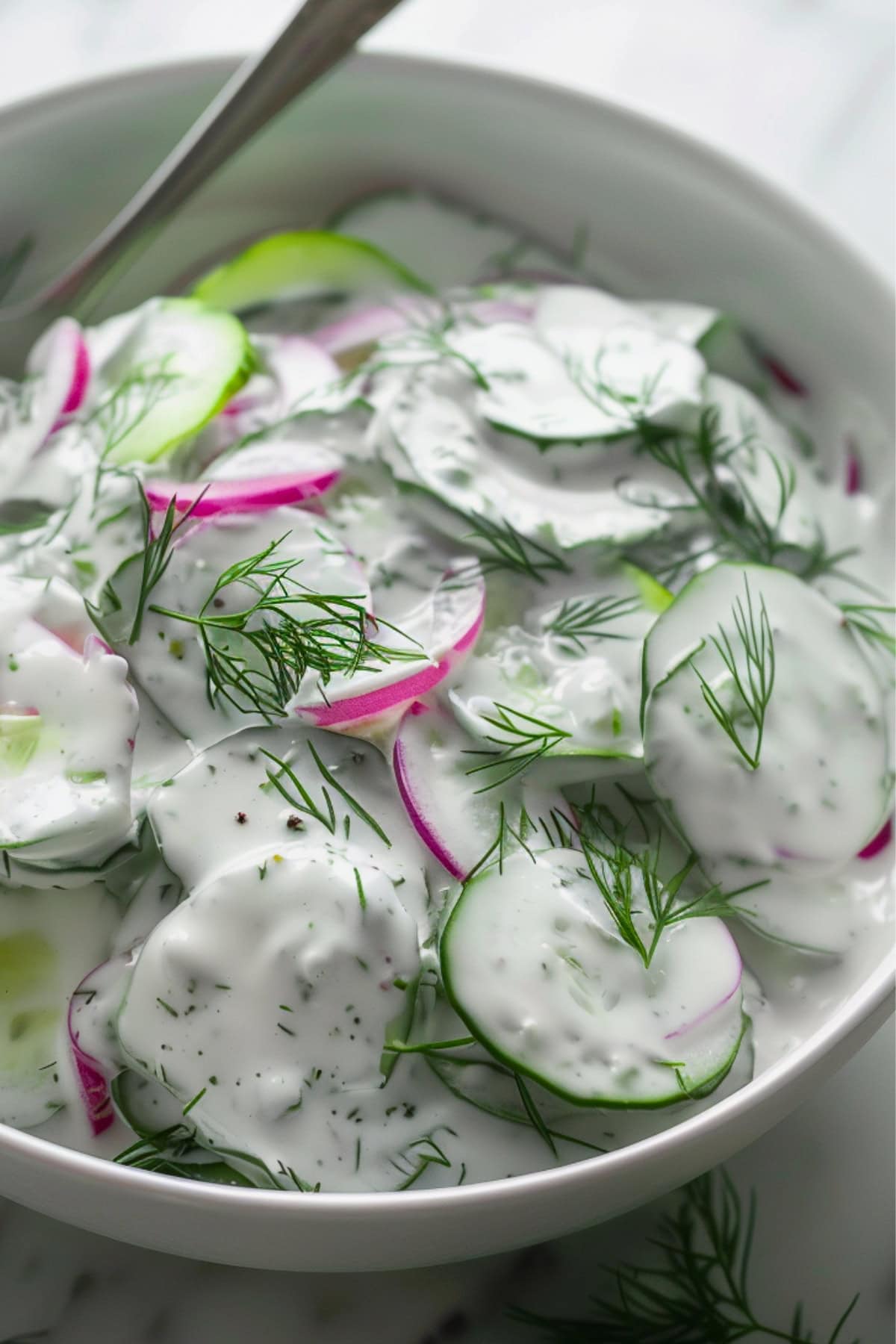 Creamy cucumber salad serving in a white bowl.
