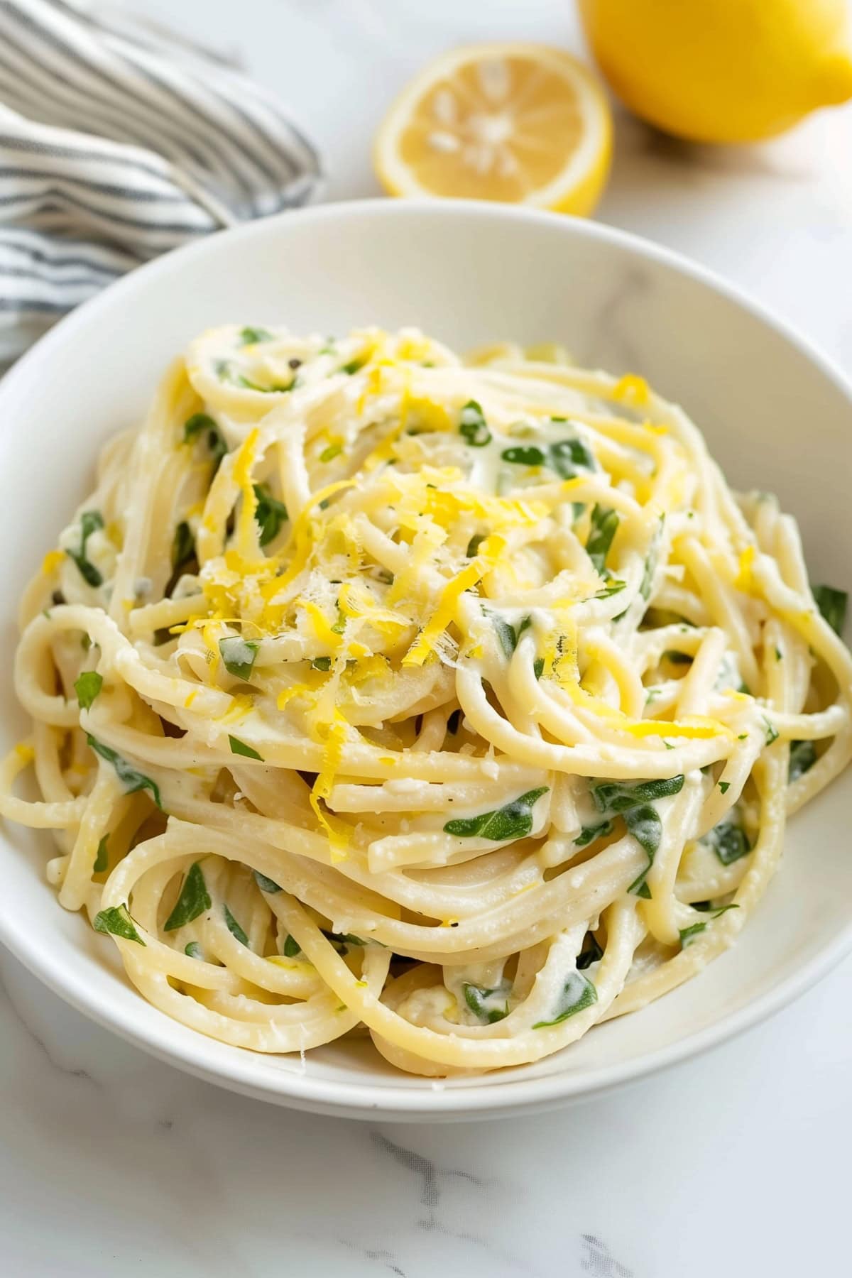 Creamy lemon ricotta pasta, featuring zesty lemon zest and baby spinach in a white bowl.