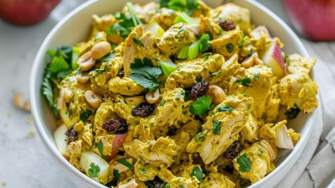 Chicken curry salad with curry spices, sweet raisins and apples, crunchy cashews, and fresh cilantro served in a white bowl.