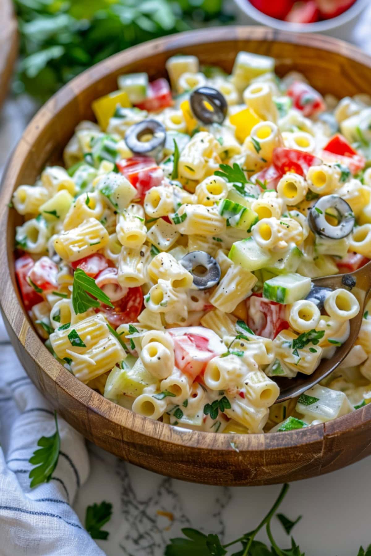 Serving of pasta salad made with ditalini pasta, cherry tomatoes, cucumber, bell pepper, and red onion and creamy dressing served in a wooden bowl.